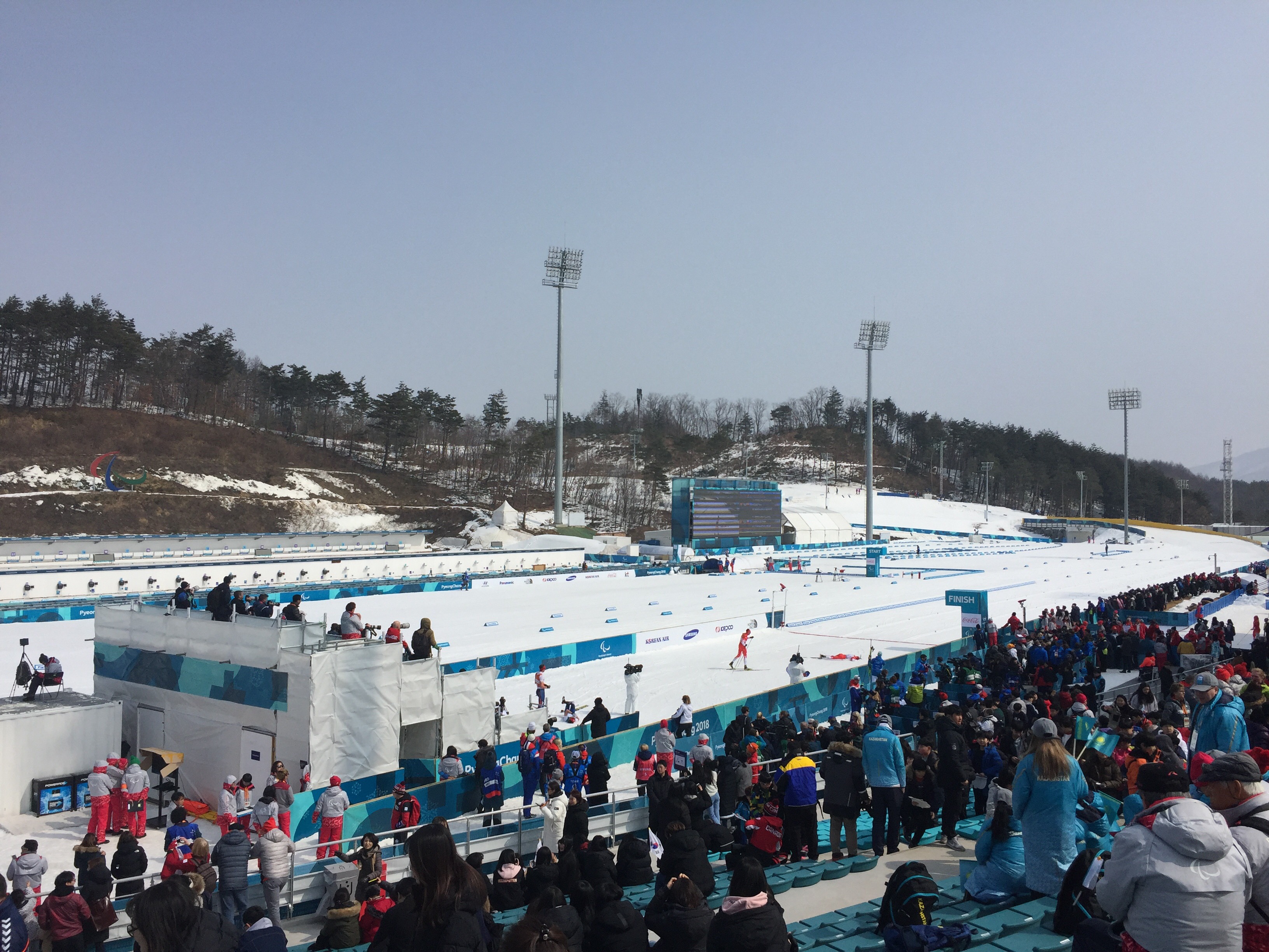 Spectators watch the track for Nordic events under a clear blue sky.