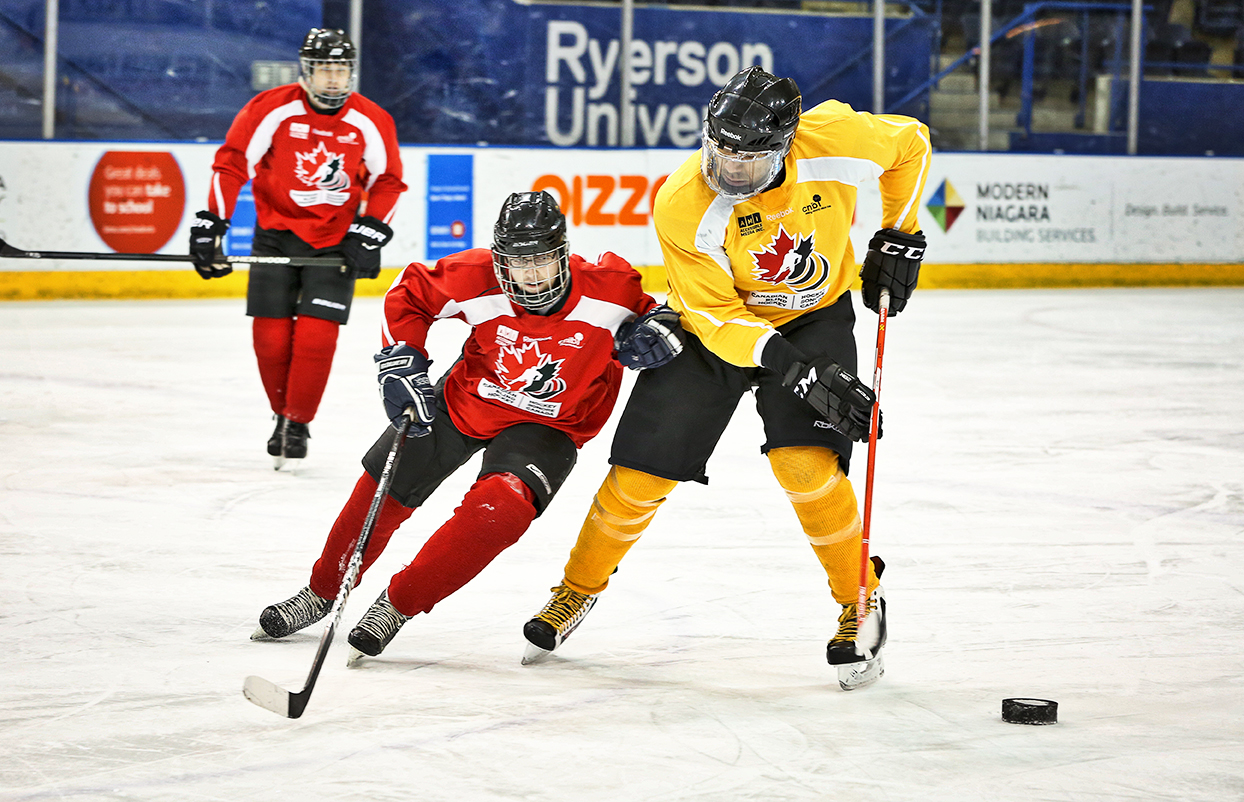 Two players, one red and one yellow vie for the puck on the ice.