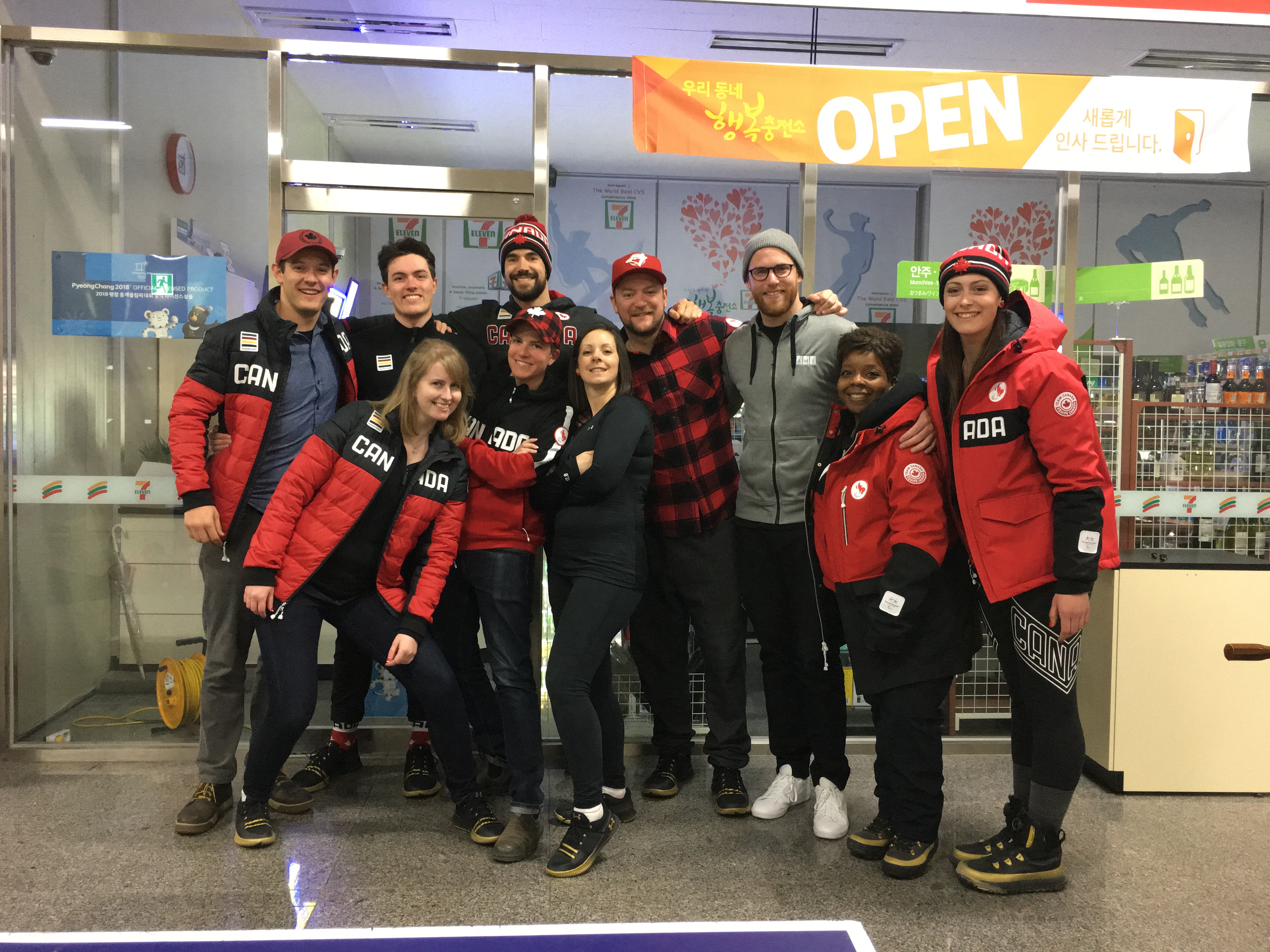A group of media personnel posing for a photo including Anthony McLachlan and Matthew McGurk and Emily Harding from Accessible Media Inc. Many in the photo are wearing team Canada gear.  