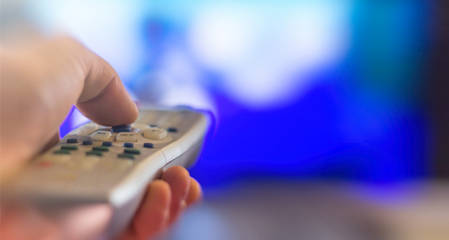 A hand holds a television remote.