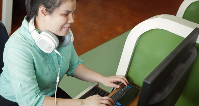 Young blind woman using computer with refreshable braille display