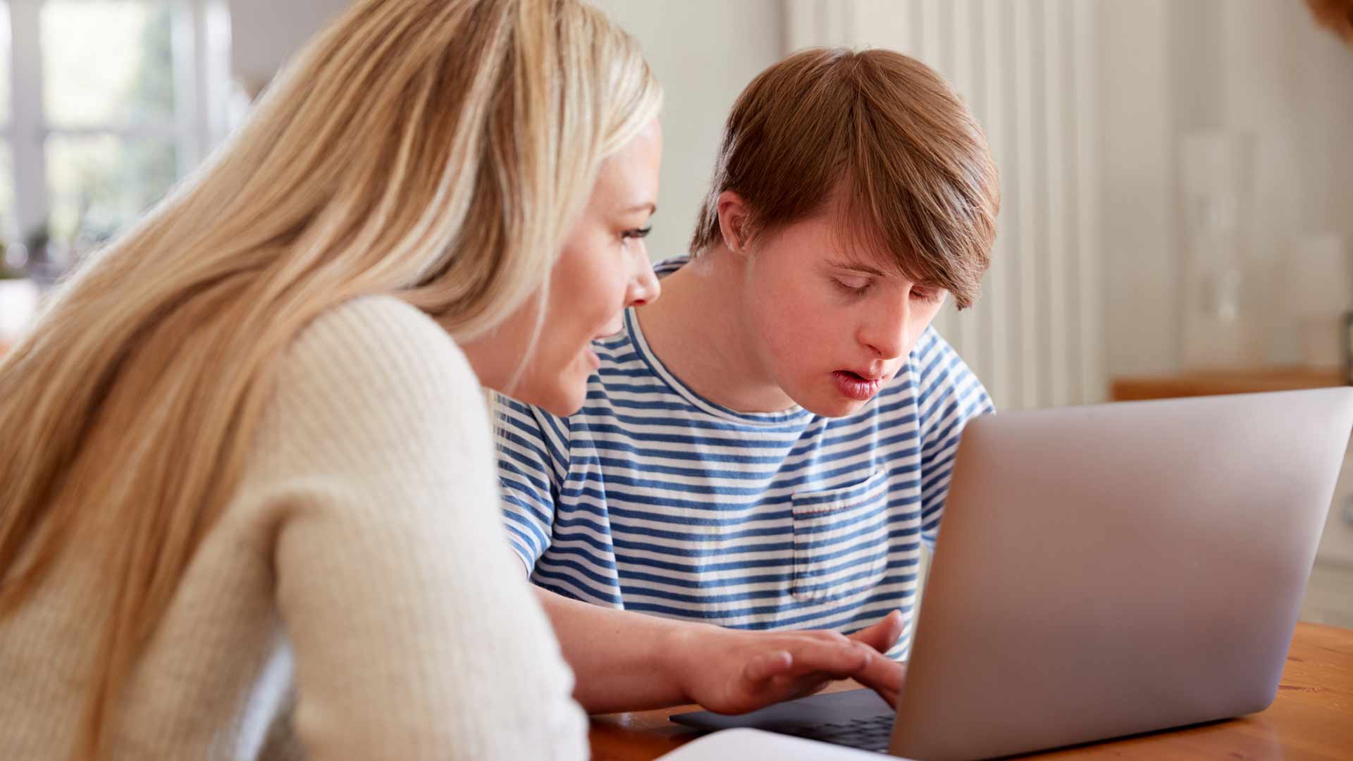 Man with down syndrome sits with a tutor as he works on a computer. 