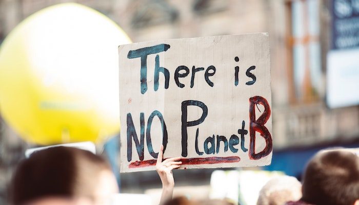 A perso's hand holds up a sign that reads "There is no planet B."