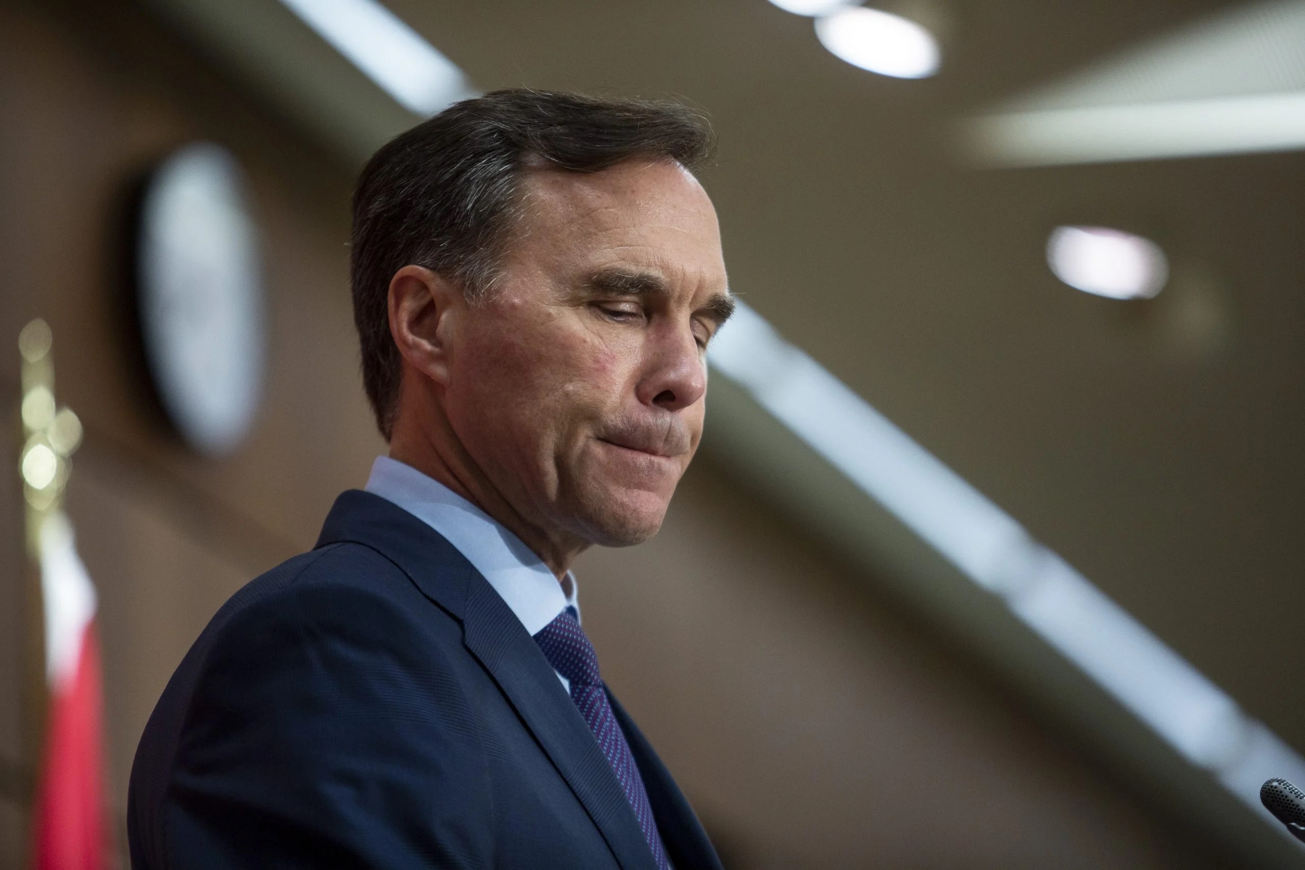 A photo of Bill Morneau wearing a suit and looking downward with his lips pursed.
