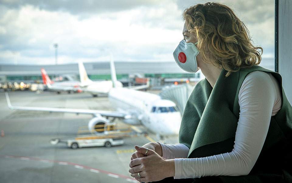 A woman wearing a face mask look out an airport window with planes in the background.