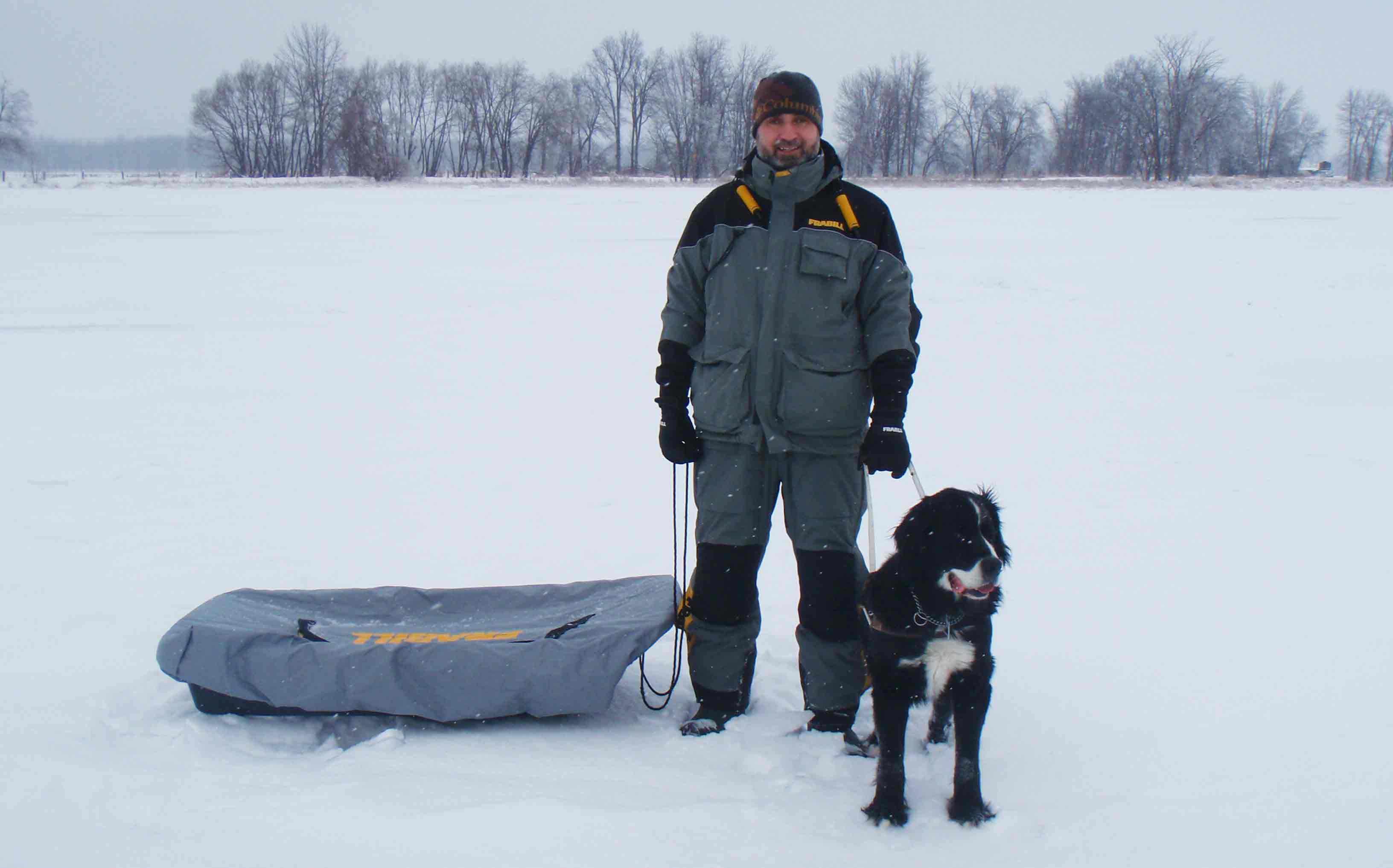 A man and a guide dog stand on a frozen lake. The man is wearing winter gear.