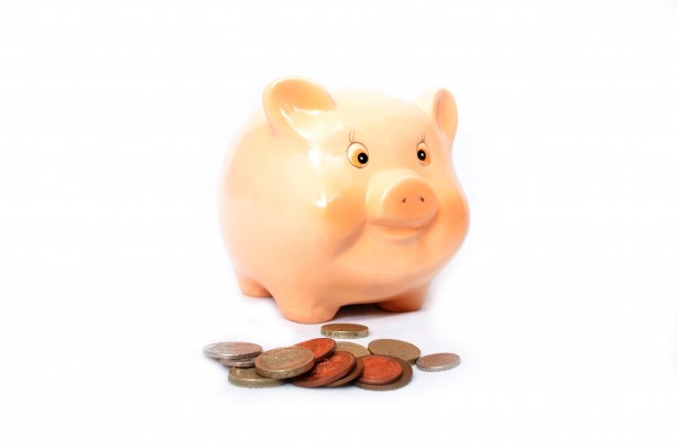 A pink piggy bank centred on a white field with a small stash of coins in the foreground 