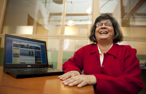 A woman wearing a red jacket laughs while sitting beside a laptop computer. Image source: Global Accessibility News.