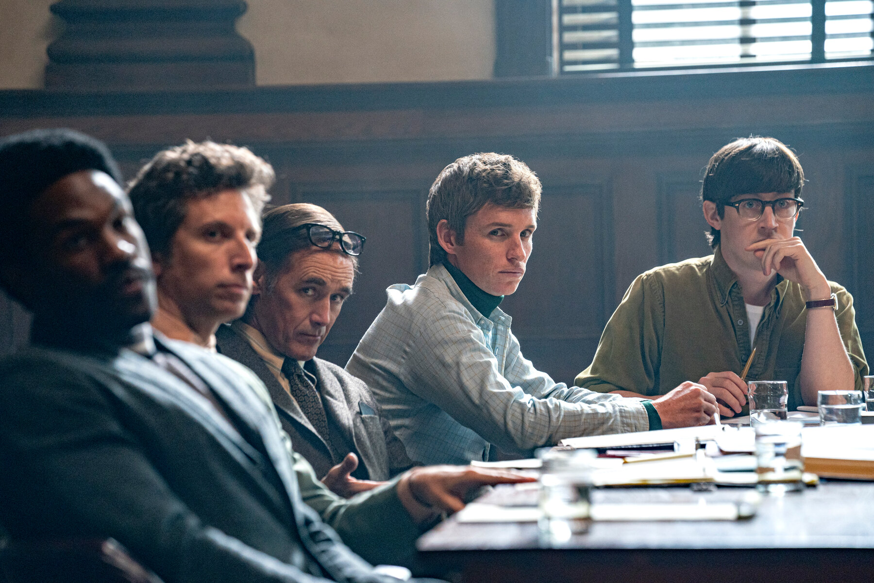 A scene from The Trial of the Chicago 7 where five men sit at a court table.