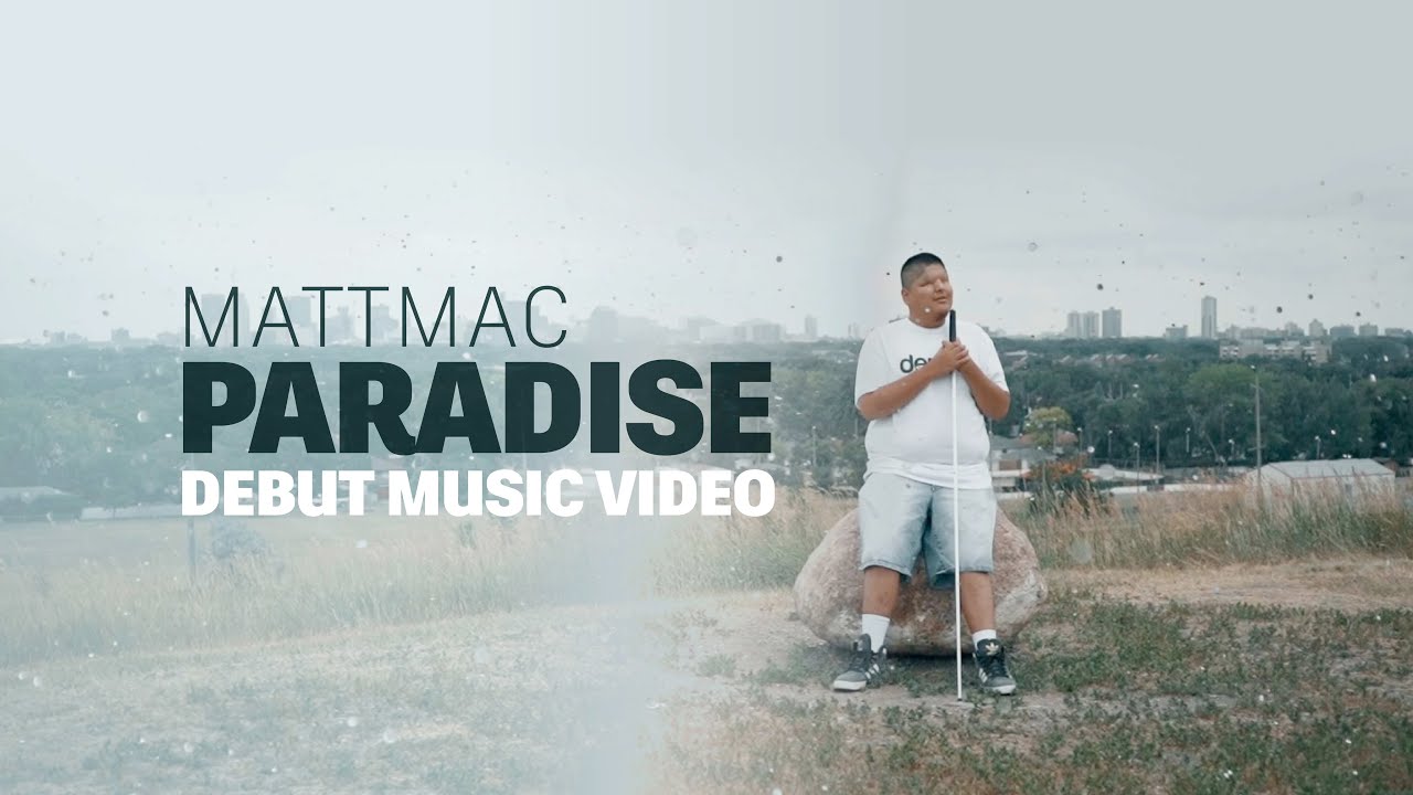 A young Indigenous man (Mattmac) clad in a white t-shirt and shorts leans back against a boulder while holding a white cane. Behind him lies the skyline of the city of Winnipeg. Text reads “Mattmac Paradise Debut Music Video” 