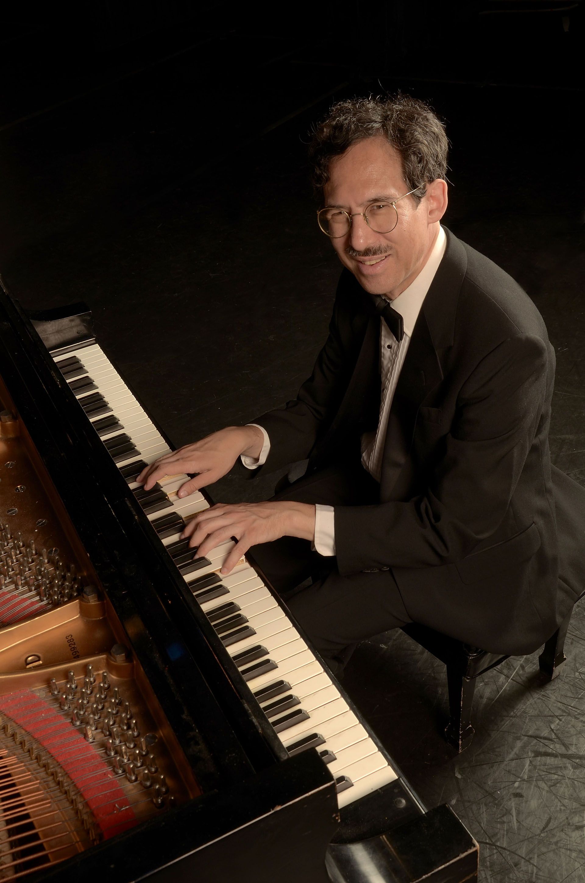 A photo of pianist Michael Arnowitt playing piano while wearing a suit. 