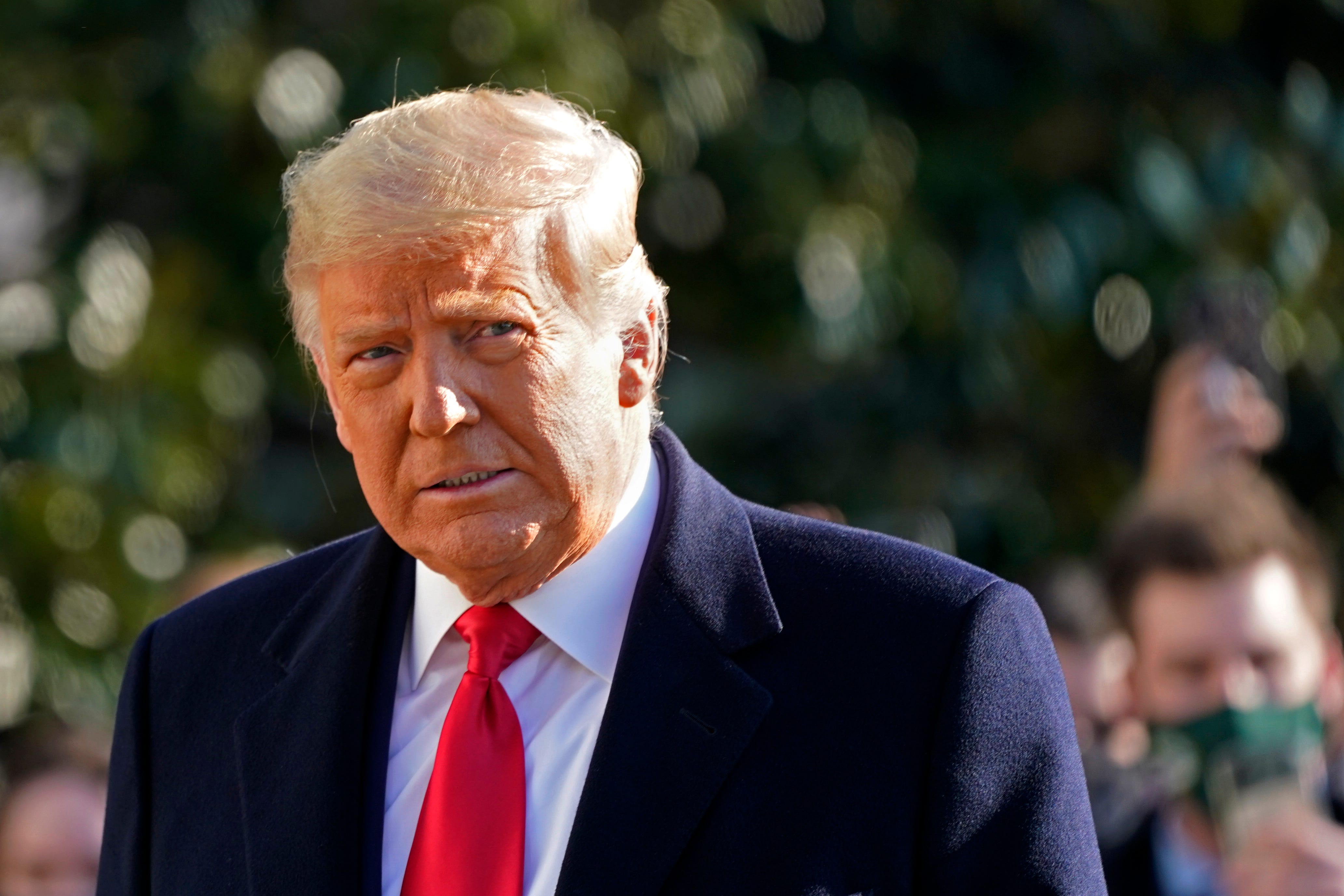 A photo of Donald Trump outisde in a suit with a red tie.