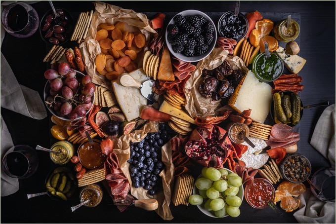 Image shows a giant charcuterie board from above. On the board are a wide variety of fruits, cheeses, spreads, and crackers. Image credit: Jules Sherred