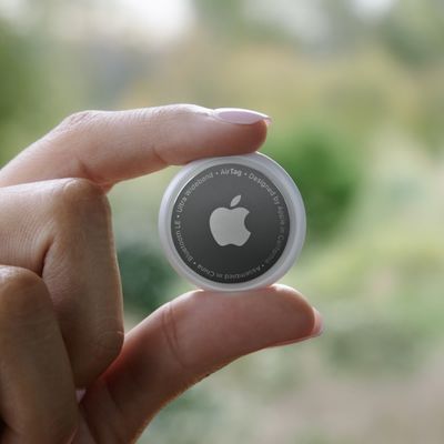 A closeup of a person holding a circular Apple Airtag, the size of a toonie. 