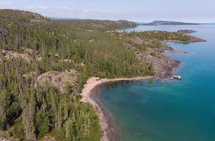 A photo of land covered in tall green trees alongside a blue lake.