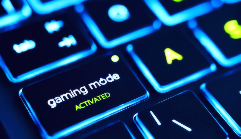 a glowing keyboard is in extreme focus, letters on the keys are blurred out save for one that reads: "gaming mode activated" 