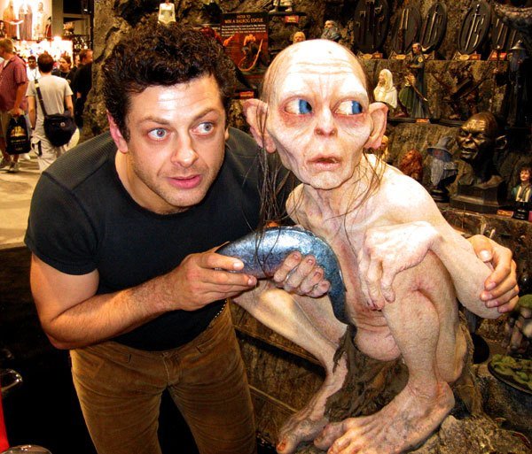 Actor Andy Serkis poses wide-eyed and arms around a sculpture of Gollum from Lord of the Rings at a convention