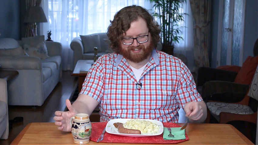Alex Smyth, smiling, prepares to eat a plate of potato salad and sausage
