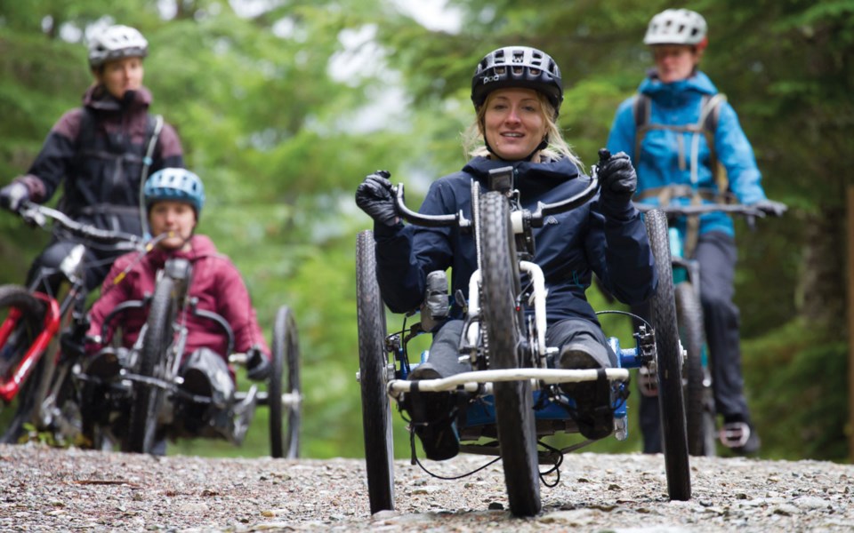 four women are seen dressed in mountain outerwear. two of them riding mountain bikes and two riding adaptive mountain bikes