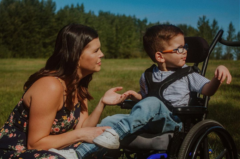 Meranda and Vincent sit in a field. Vincent is a power wheelchair user.