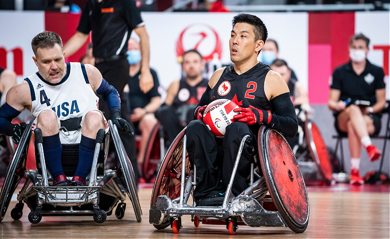 Travis Murao holds a wheelchair rugby ball in his hands. 