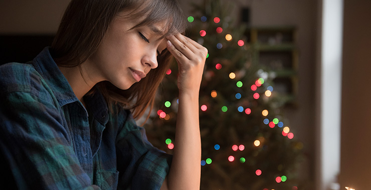 A woman looking stressed by a Christmas tree