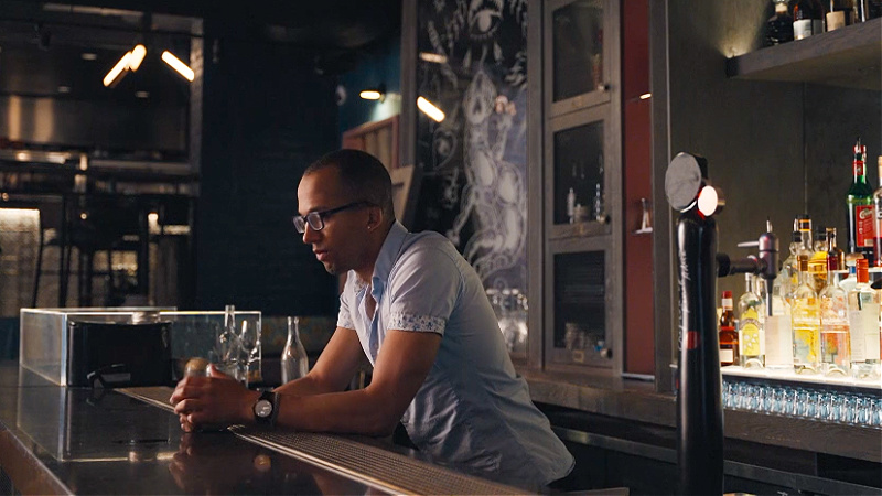 Caeden behind a bar with a wall of booze behind him.