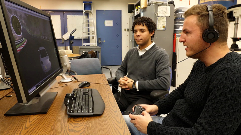 Two men, seated at a desk, look at a computer screen.