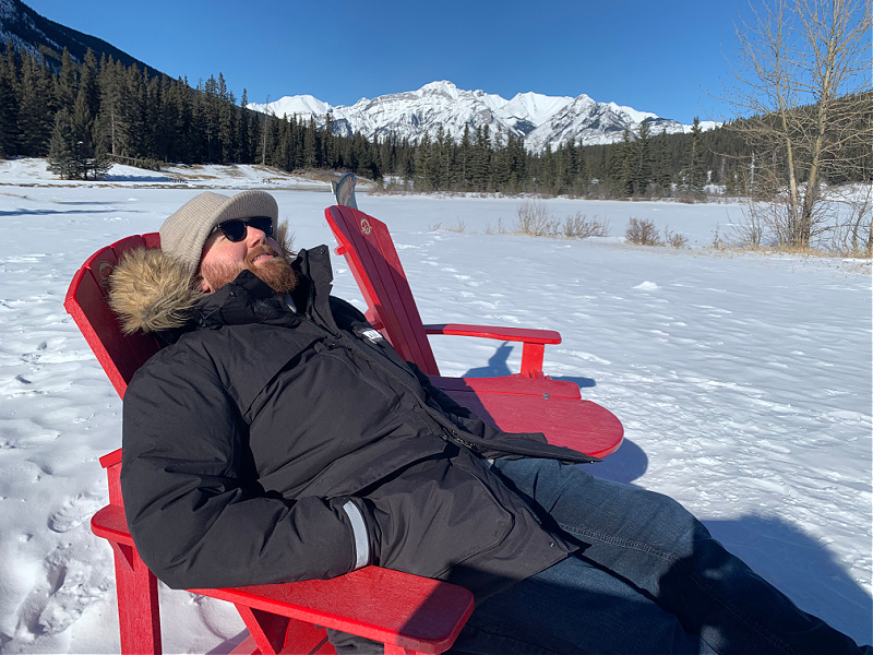 Alex Smyth, dressed in a winter coat, relaxes on an Adirondack chair.