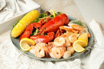 A plate with a full lobster, shrimp, potatoes and corn on it.