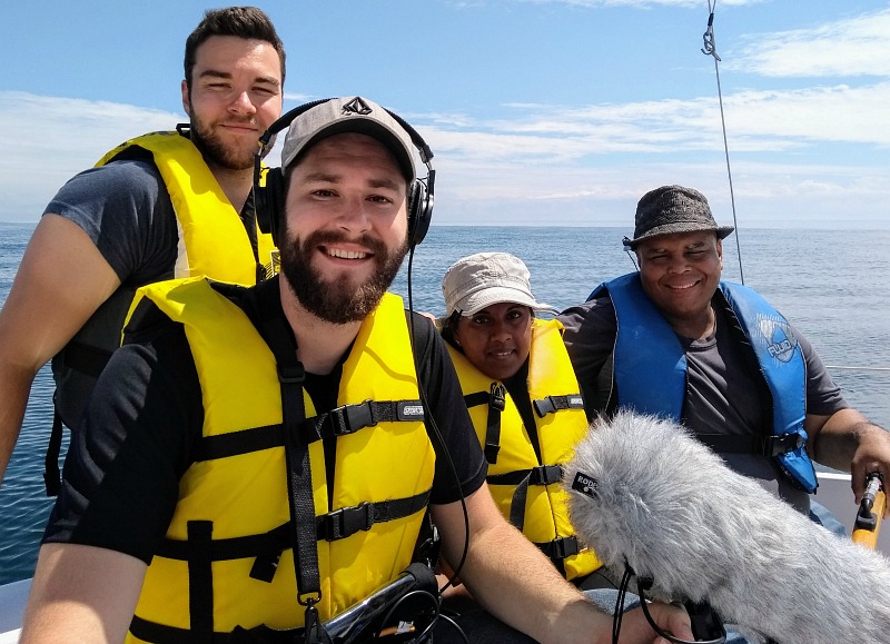 Four people sit in a sailboat, wearing life vests.