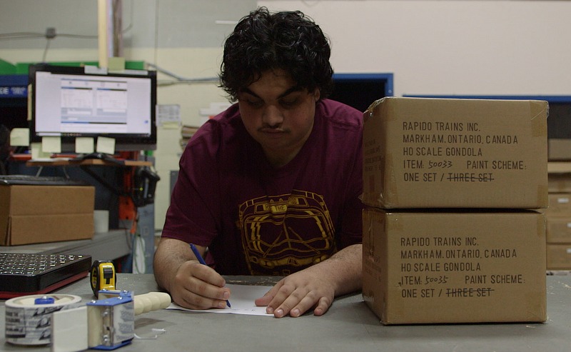 A man sits at a desk, writing on a piece of paper with a pen. 