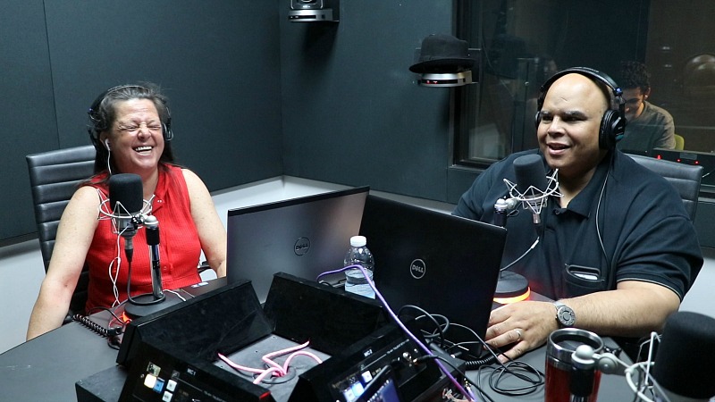 A woman laughs while sitting next to a man in a radio studio.