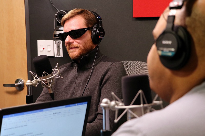 A man sits in a radio studio, wearing headphones.