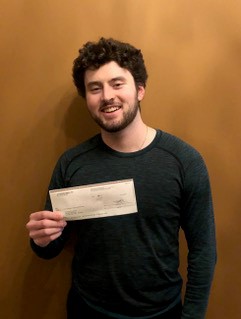 A man smiles into the camera while holding a cheque in his hand.