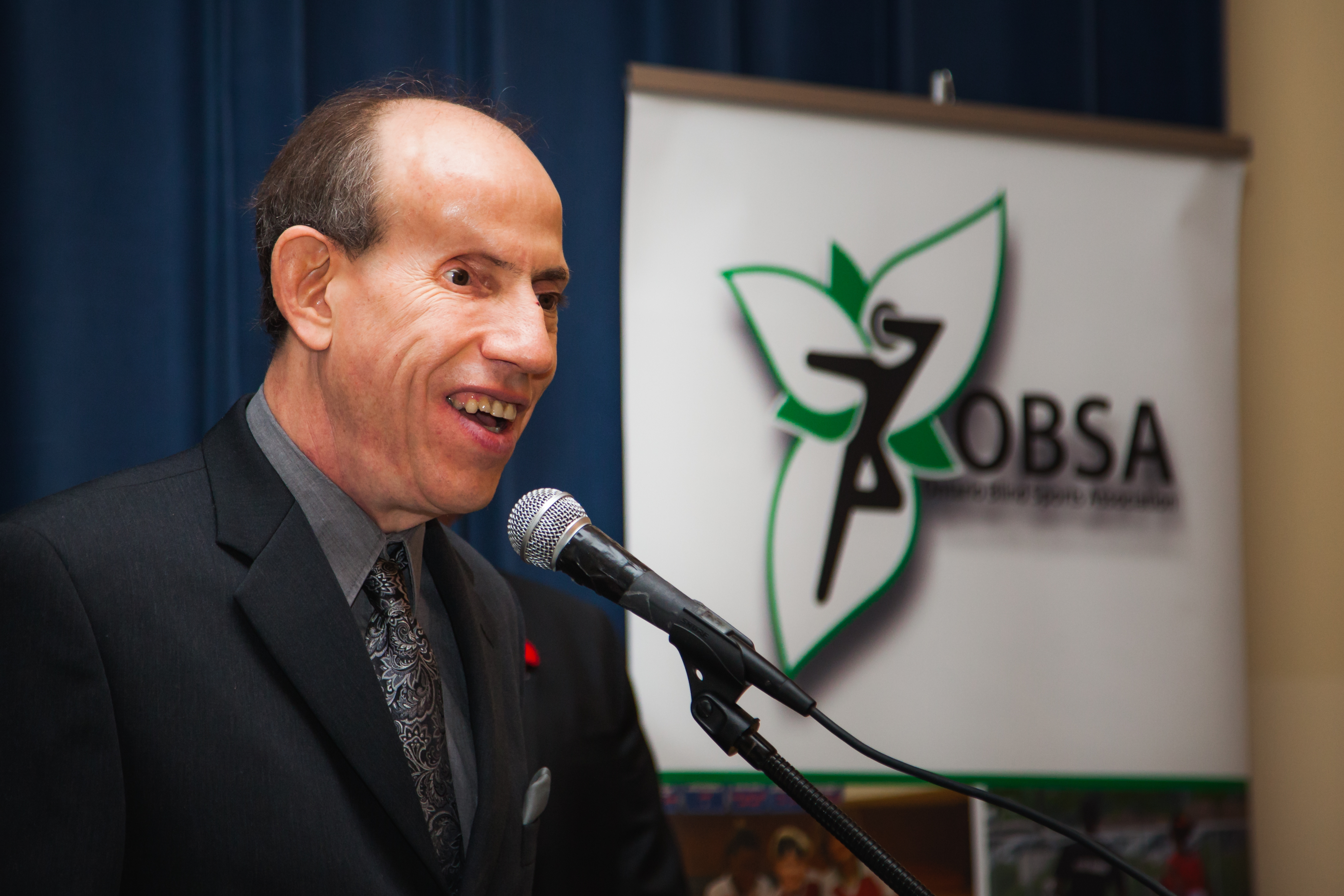 An award recipient is at a podium giving an acceptance speech. To his left we see the OBSA logo.  