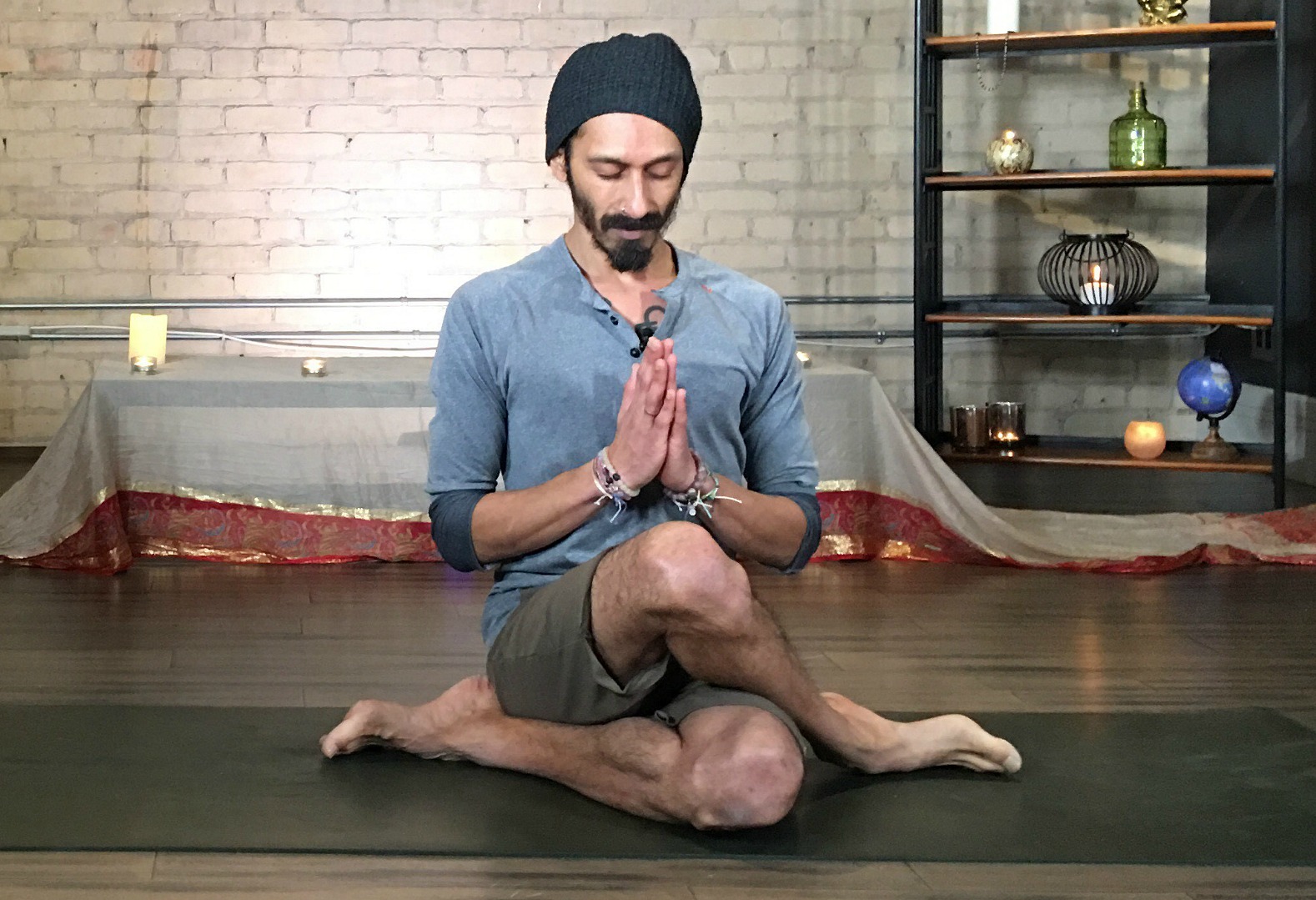 Kevin Naidoo sits on a yoga mat. His legs are crossed. His eyes are closed.