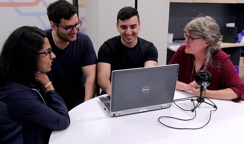 A group of people sit at a desk looking at a computer screen.