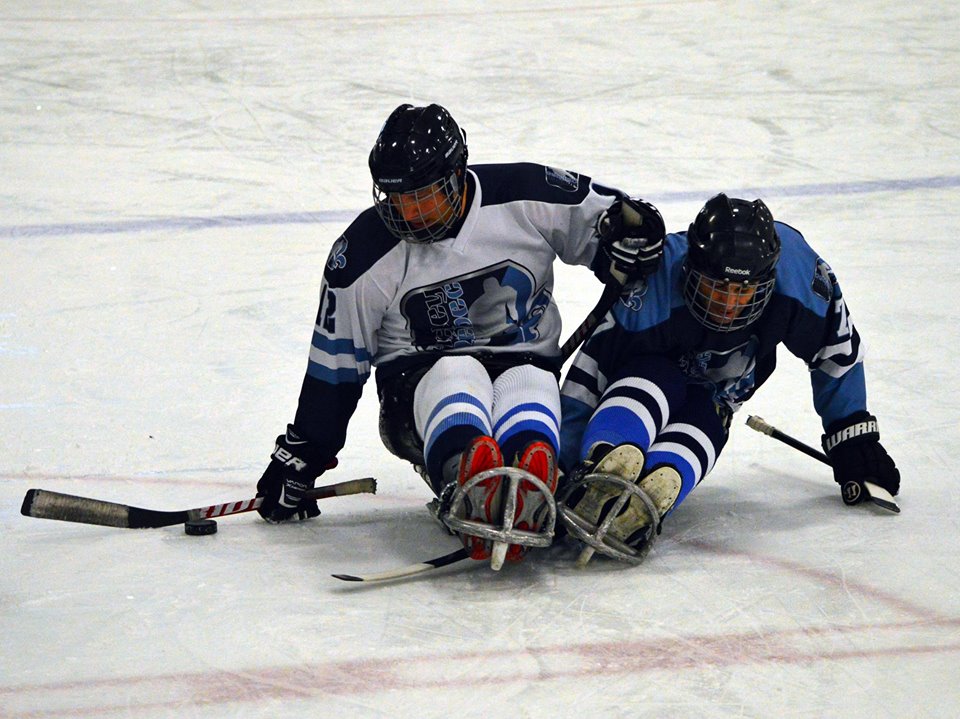 Two sledge hockey players fight for the puck.