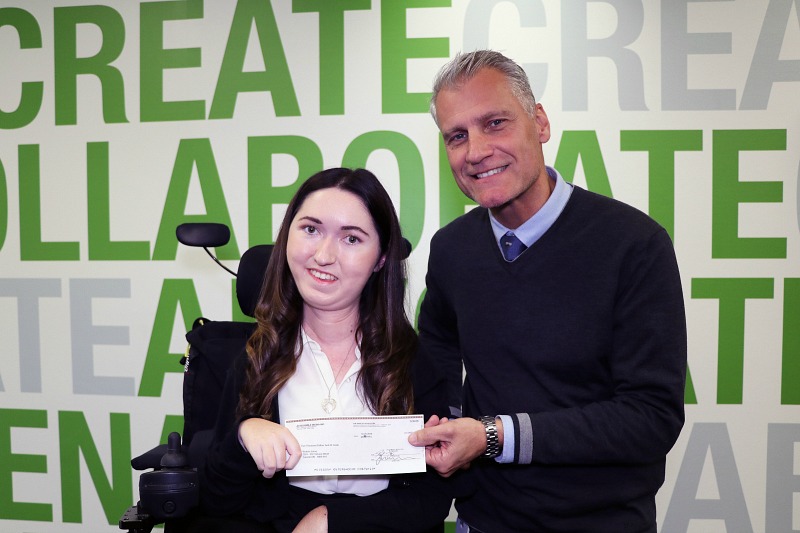 A woman and man smile into the camera. They are holding a cheque.