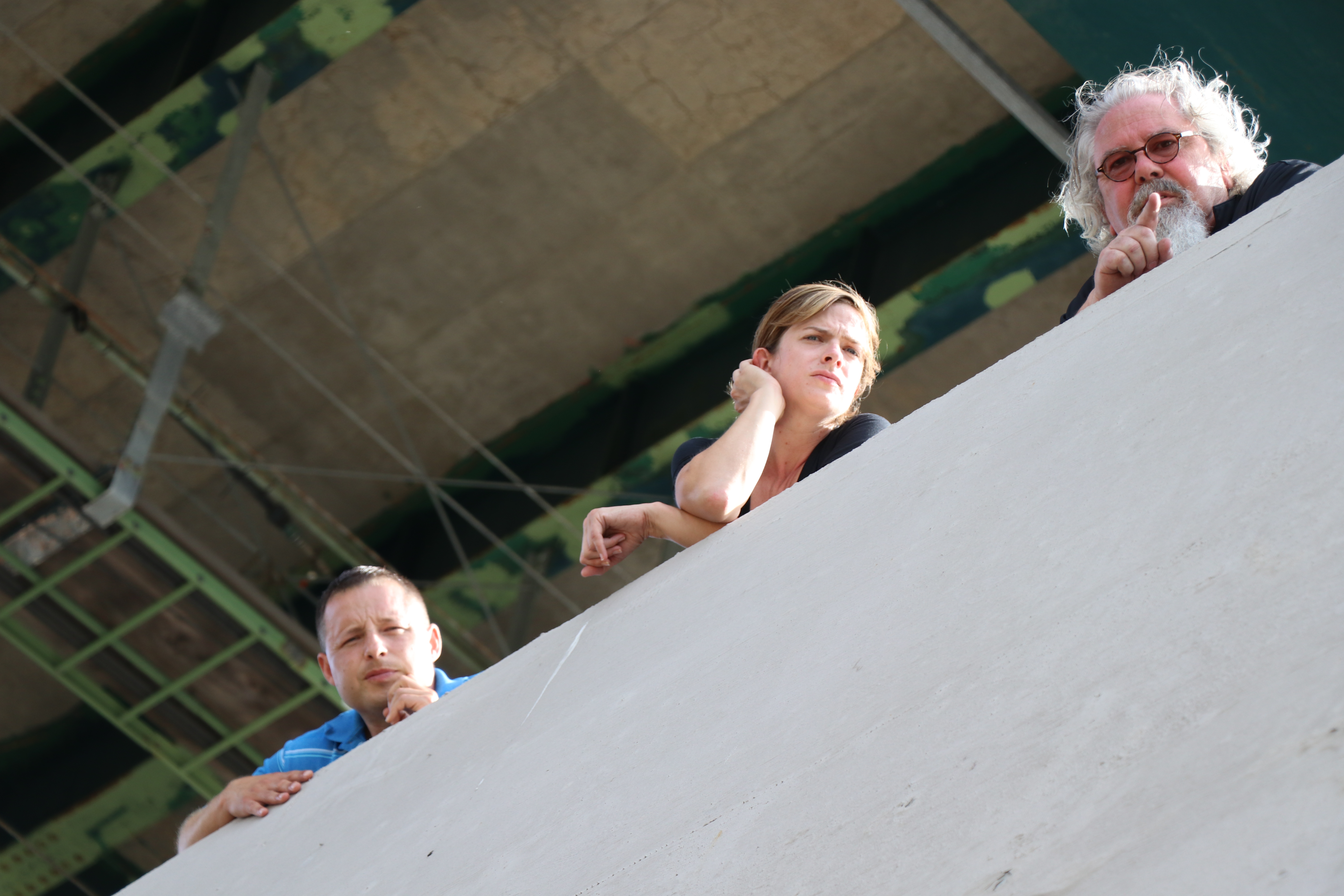 Three people look over the edge of a concrete bridge abutment.