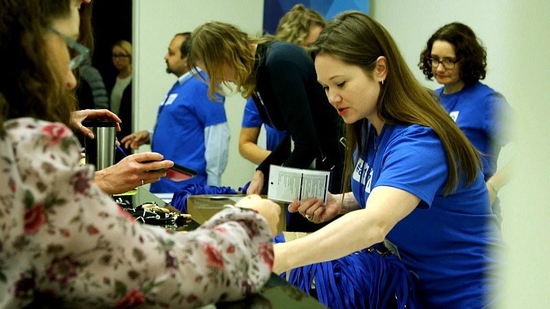 People wearing blue shirts hand out lanyards.