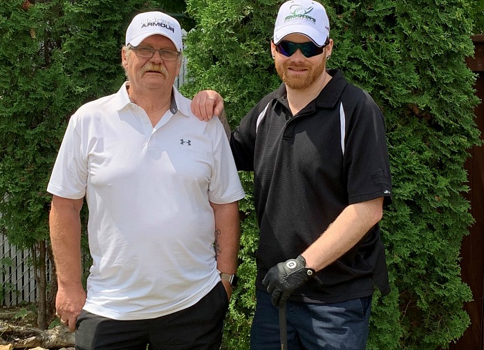 Two man stand, looking at the camera. One hold a golf club.