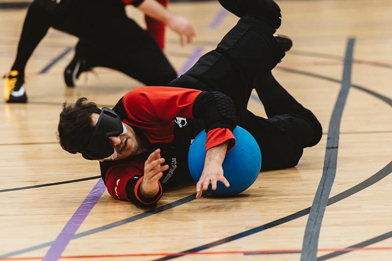 A goalball player makes a save on the court. He is wearing a blindfold over his eyes.