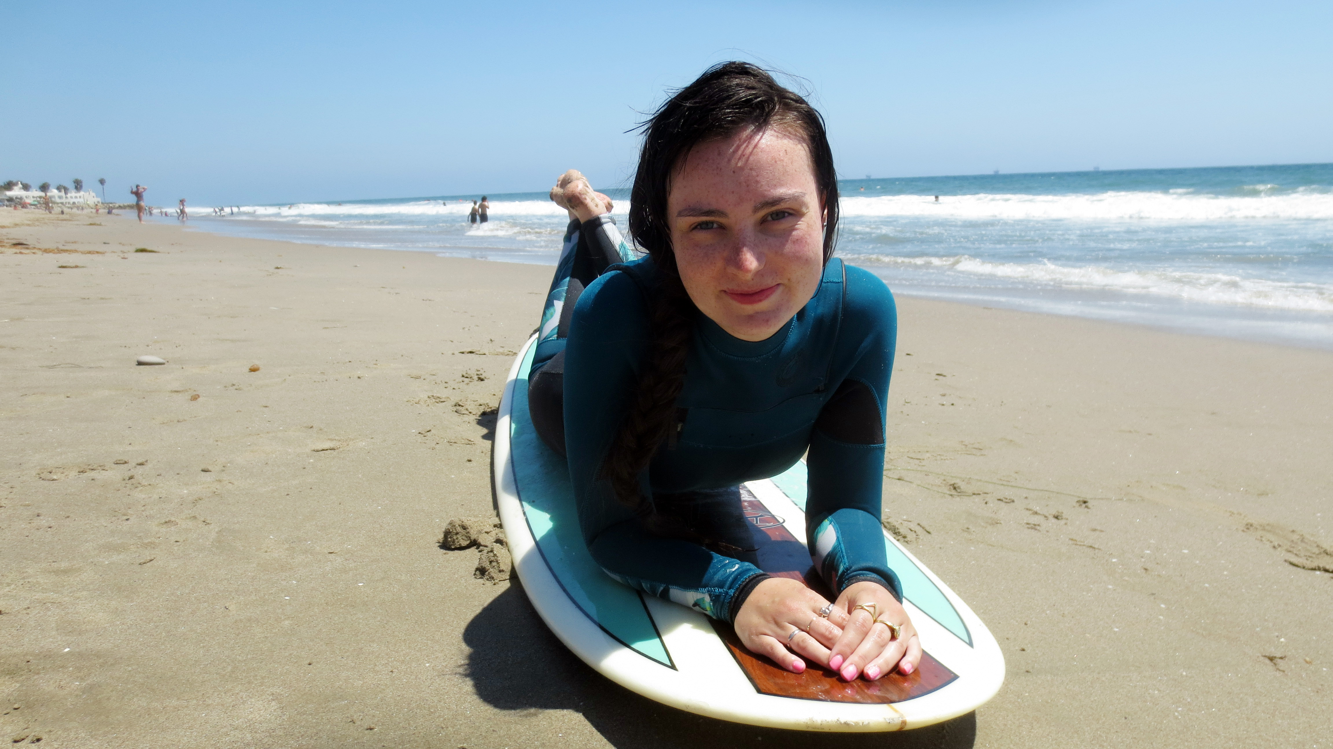 AMI This Week’s Molly Burke lies on her surfboard on a sunny California beach wearing a stylish Billabong wetsuit, waves lapping in the background.