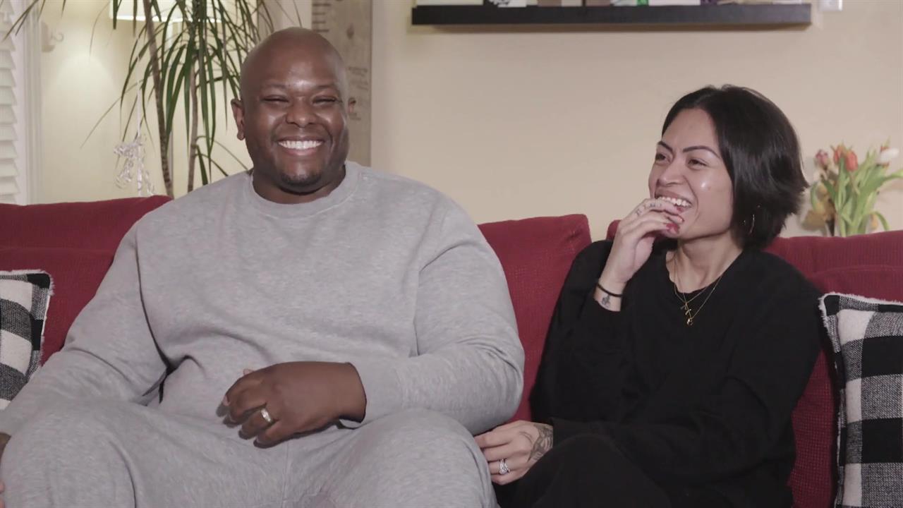 A man and woman sit on a couch, laughing.