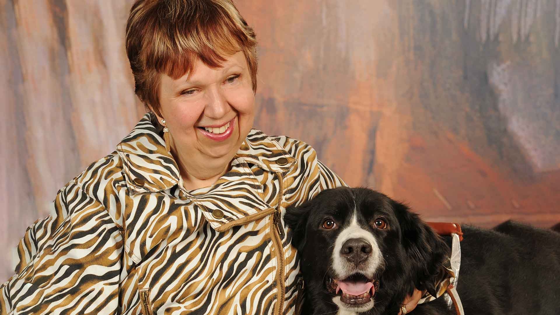 A woman and her guide dog smile into the camera.