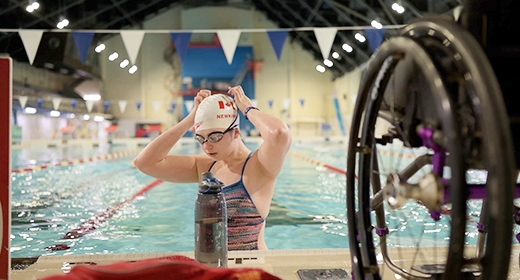A woman stands in a swimming pool, adjusting her cap.