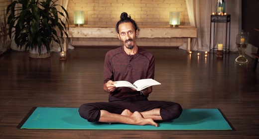 Kevin Naidoo sits cross-legged on a rug, holds a book