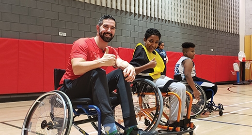 Two people, using wheelchairs, smile into the camera, with thumbs up.